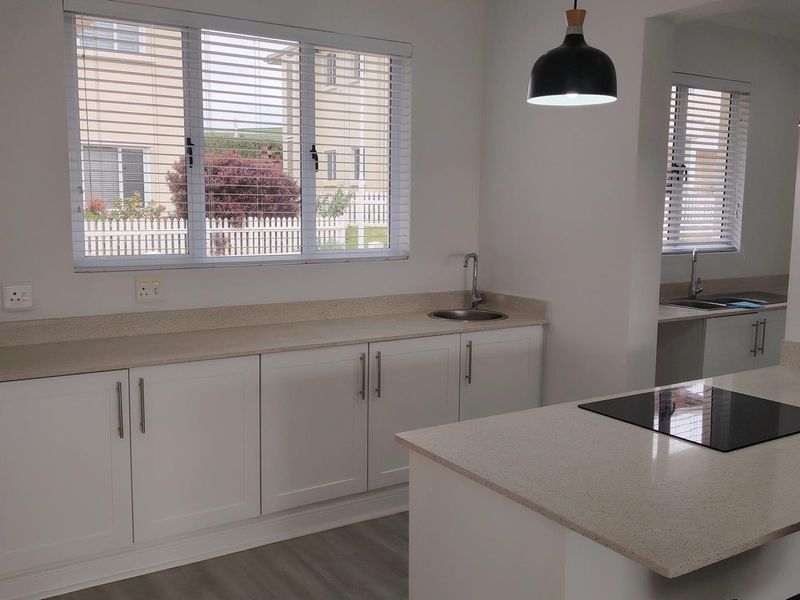 Modern kitchen featuring white cabinetry, stone countertops, an integrated induction cooktop, and a secondary prep area with a sink.