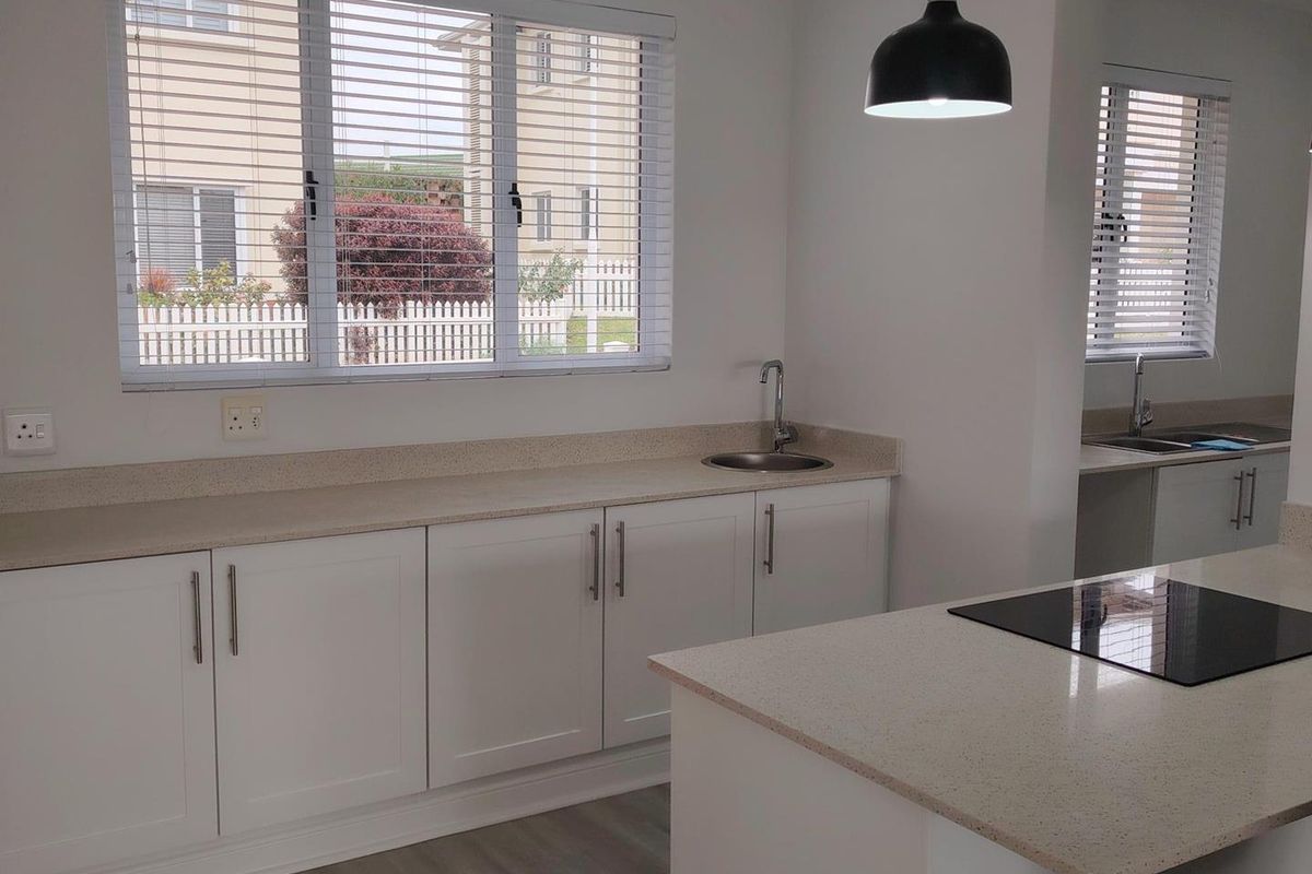 Modern kitchen featuring white cabinetry, stone countertops, an integrated induction cooktop, and a secondary prep area with a sink.