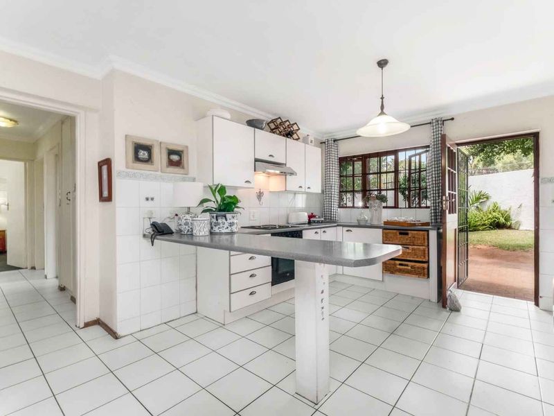 Functional kitchen featuring white cabinetry, a breakfast bar, tiled flooring, and direct access to the rear garden area.