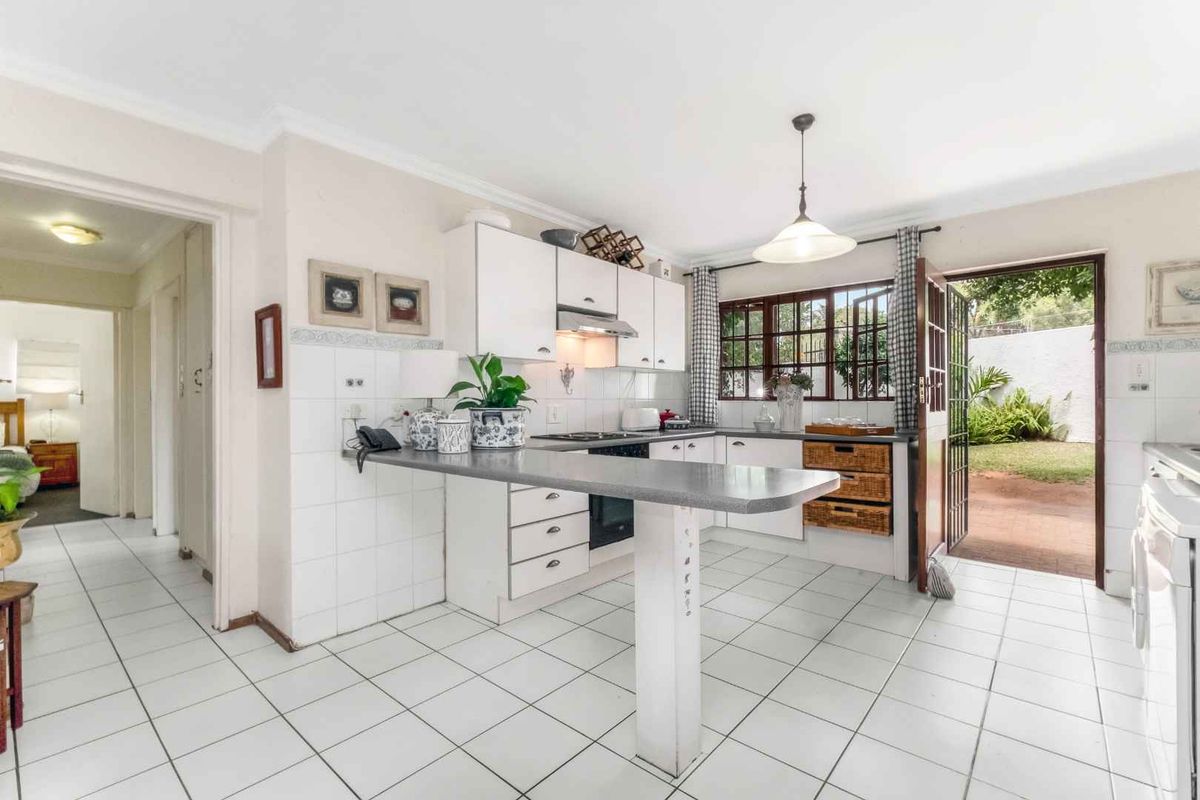 Functional kitchen featuring white cabinetry, a breakfast bar, tiled flooring, and direct access to the rear garden area.