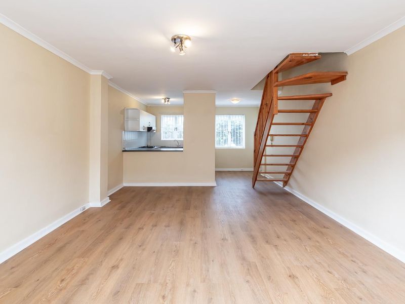 Open plan living area featuring laminate flooring, a wooden staircase, and a compact kitchen with built-in cabinetry and appliances.