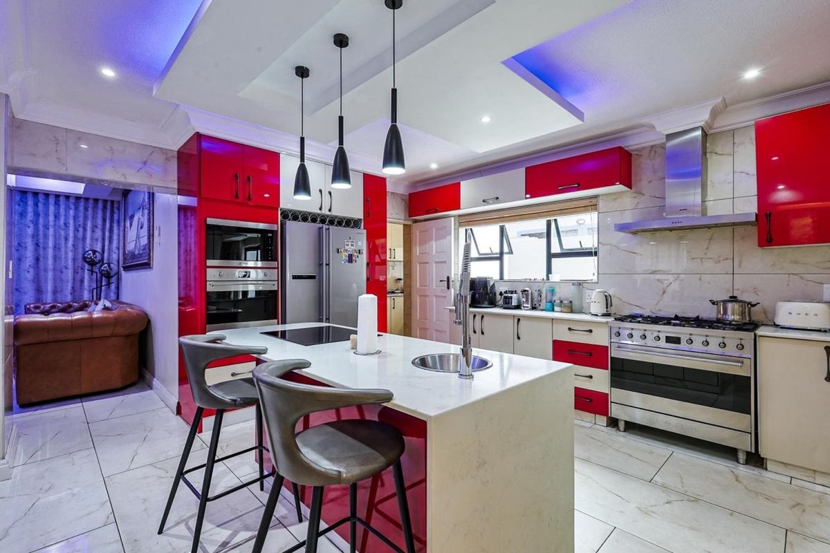 Modern kitchen featuring a central island with a built-in cooktop, high-gloss cabinetry, stone countertops, and integrated stainless steel appliances under a tray ceiling.