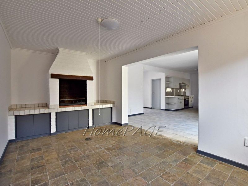 Open plan living area featuring a built-in braai and tiled flooring, flowing into a functional kitchen space with built-in cabinetry and appliances.