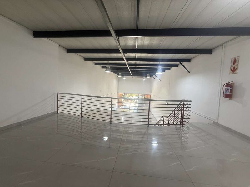 Spacious open-plan mezzanine level featuring polished tiled flooring, exposed steel ceiling beams, and industrial lighting, overlooking the lower retail area.