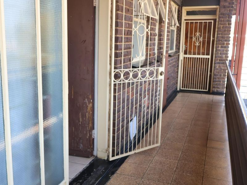 An exterior apartment balcony featuring tiled flooring, brick wall finishes, and security gates at the entrance doors.