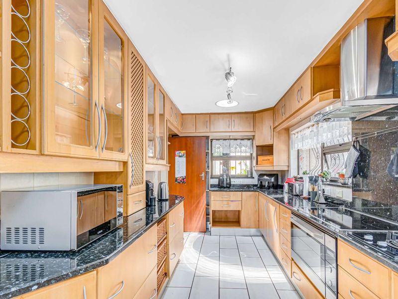 A functional kitchen featuring light wood cabinetry, granite countertops, built-in oven, gas hob, and stainless steel extractor fan with tiled flooring.