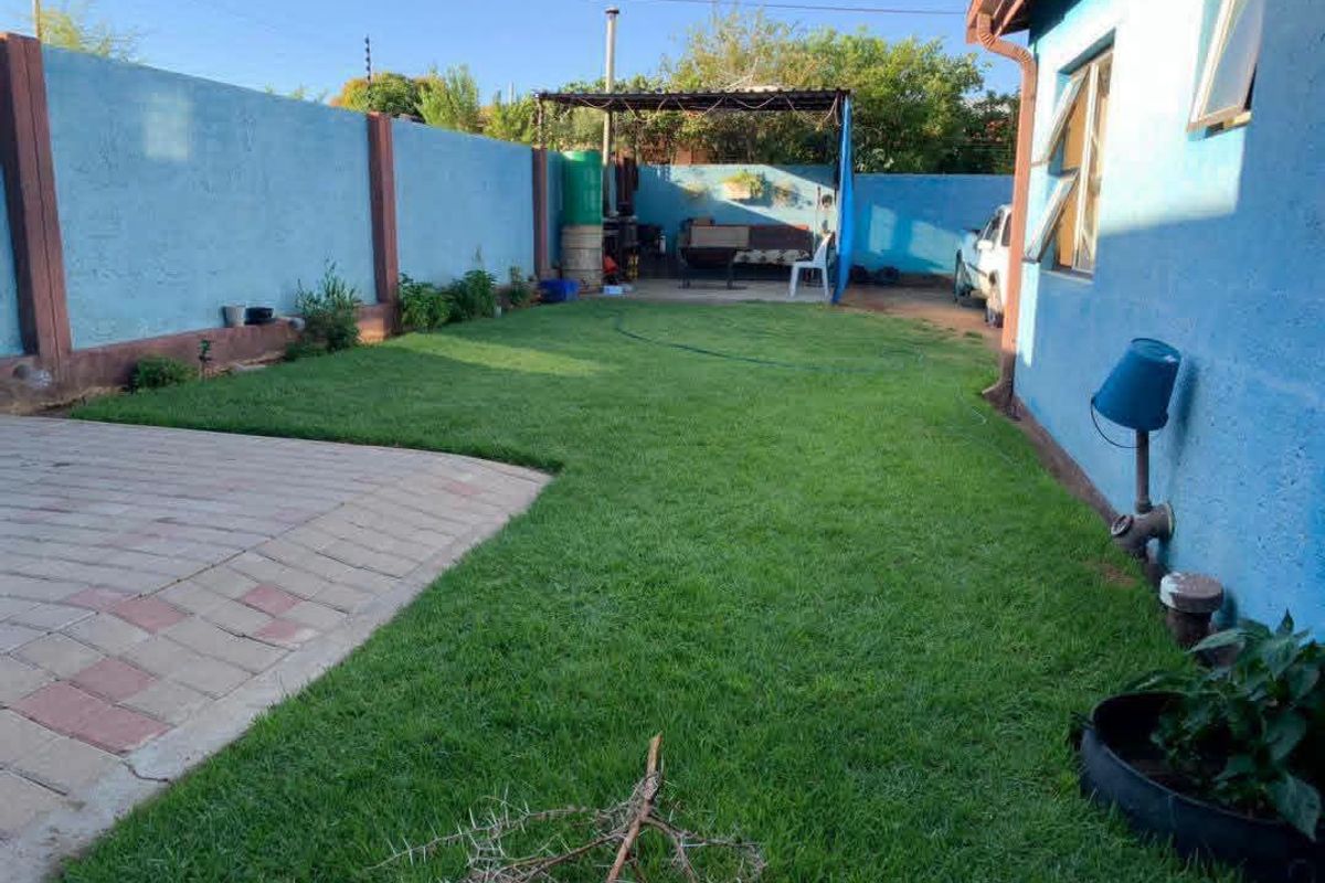 A rear garden area featuring a paved patio, a well-maintained lawn, and a perimeter wall, providing a functional outdoor space for the property.