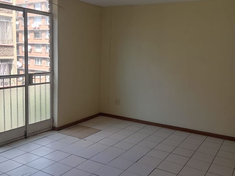 An empty living room featuring tiled flooring and a glass sliding door leading to a balcony, providing natural light and access to the exterior.