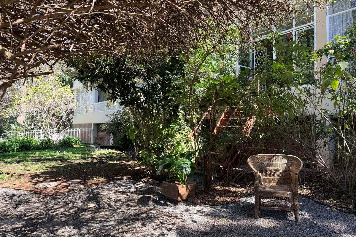 A rear garden area featuring a gravel surface, mature trees, and a timber staircase leading to the elevated apartment entrance.