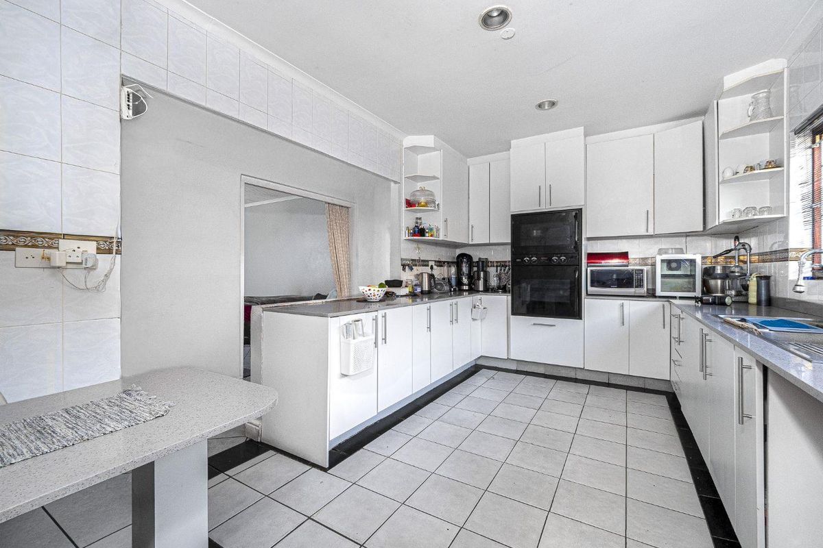 A functional kitchen featuring white cabinetry, built-in oven and microwave, tiled flooring, and a breakfast bar area.