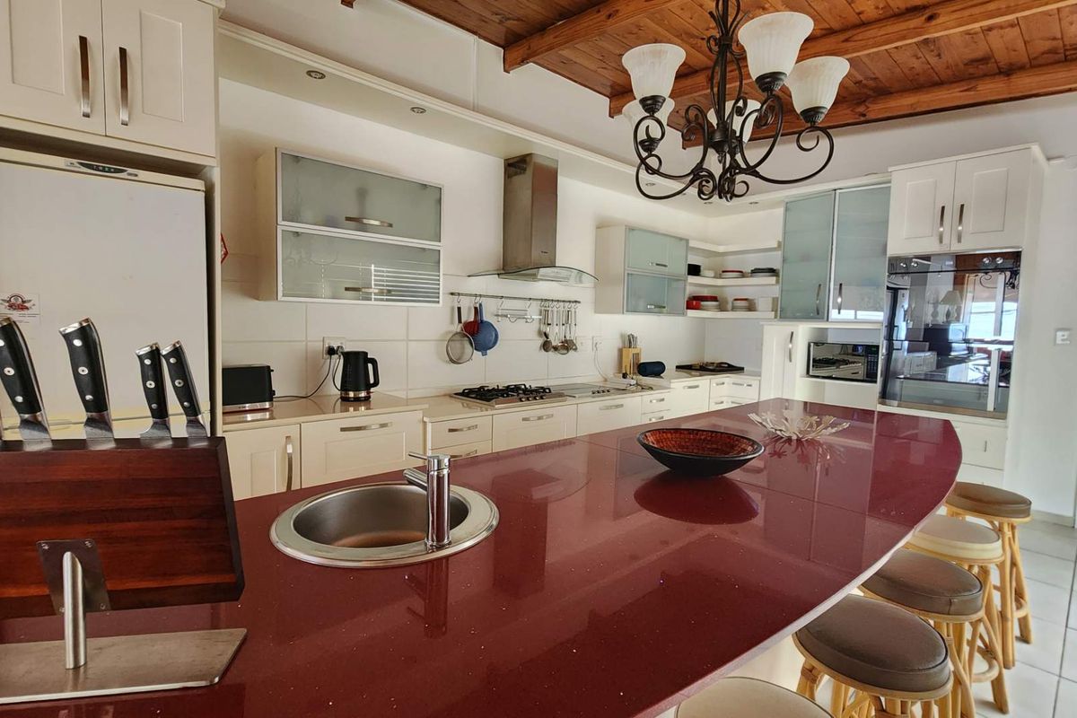 Spacious kitchen featuring a large island with a red countertop, built-in oven, gas hob, extractor fan, and timber ceiling details.