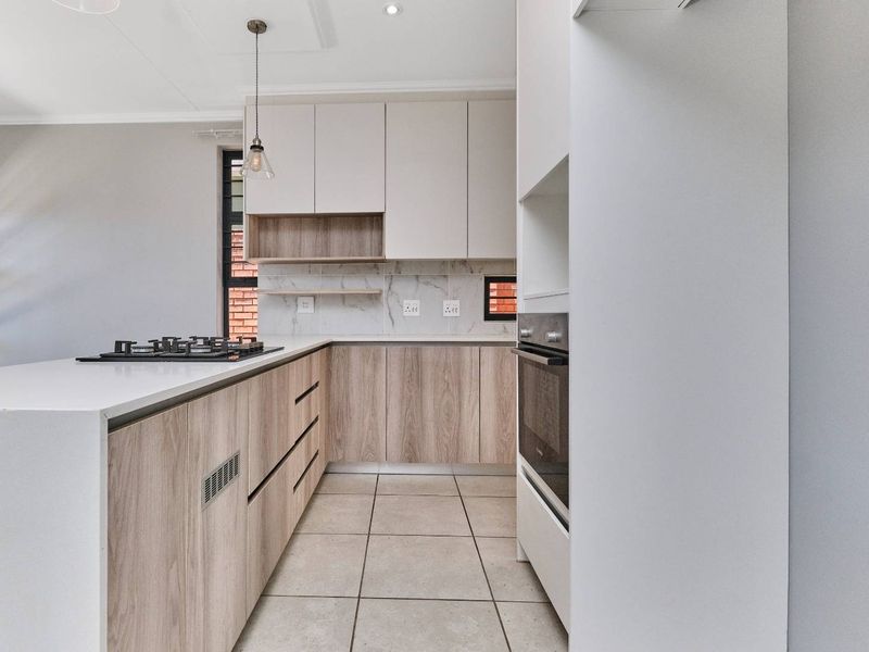 Modern kitchen featuring light wood-grain cabinetry, stone countertops, a gas hob, built-in oven, and marble-look splashback with neutral tiled flooring.