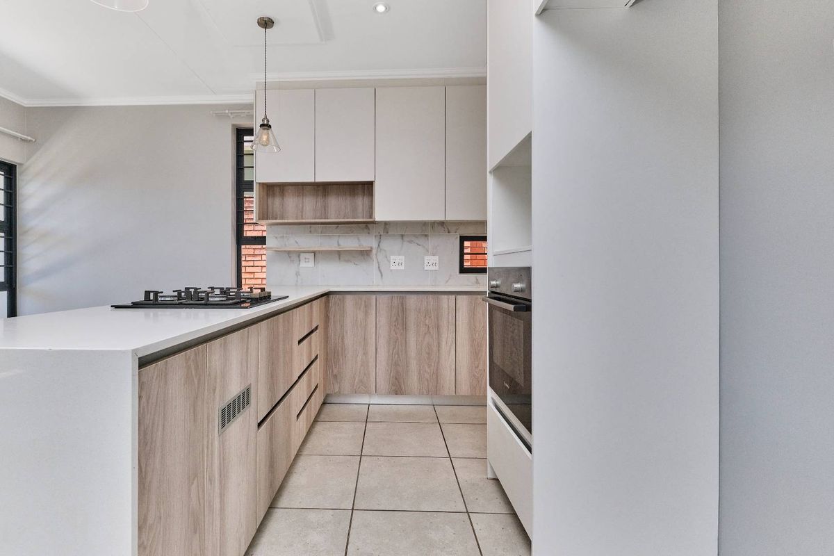 Modern kitchen featuring light wood-grain cabinetry, stone countertops, a gas hob, built-in oven, and marble-look splashback with neutral tiled flooring.
