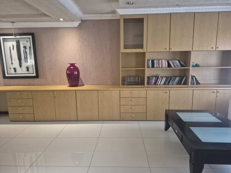A living room featuring extensive built-in light wood cabinetry, decorative crown molding, recessed ceiling lights, and polished floor tiles.