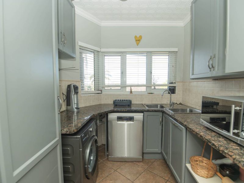A functional scullery featuring grey cabinetry, granite countertops, a double sink, and integrated space for a dishwasher and washing machine.