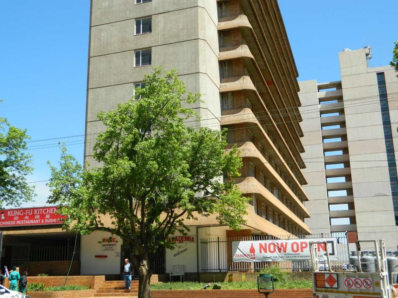 Exterior view of a multi-story apartment building featuring concrete facade, balconies, and ground-level commercial signage.
