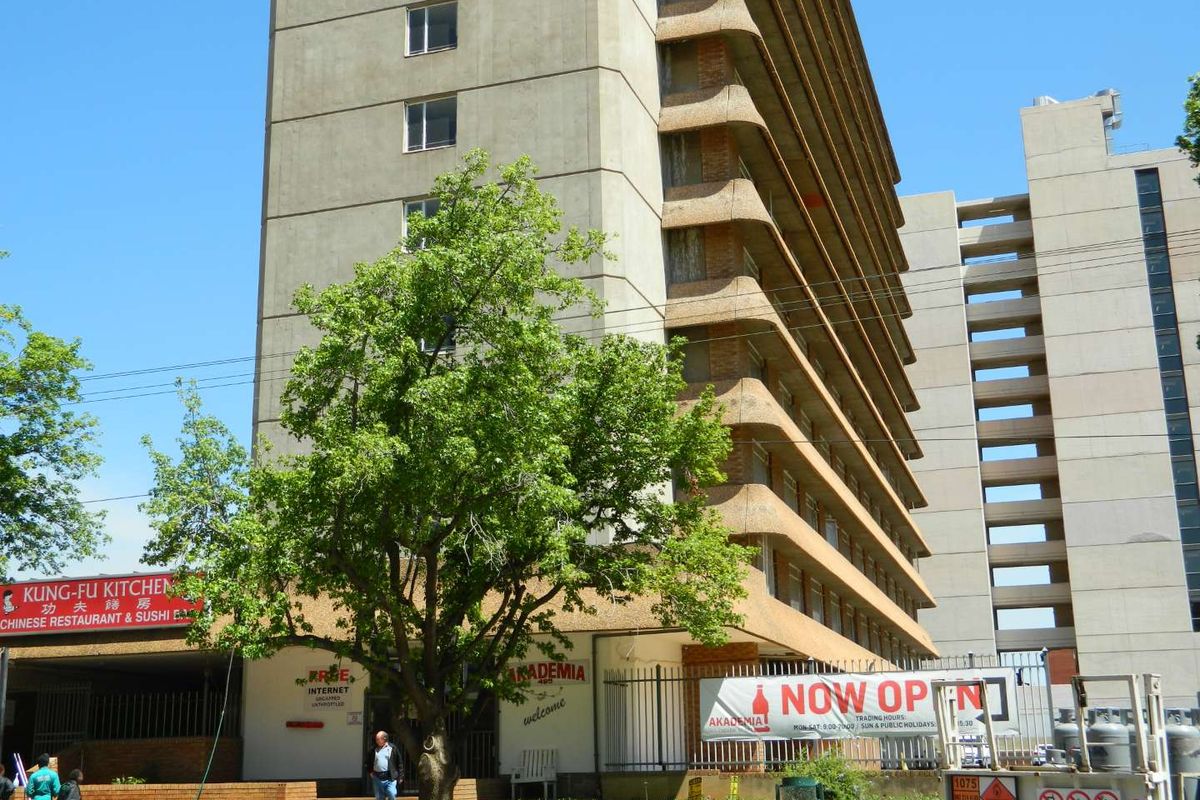 Exterior view of a multi-story apartment building featuring concrete facade, balconies, and ground-level commercial signage.