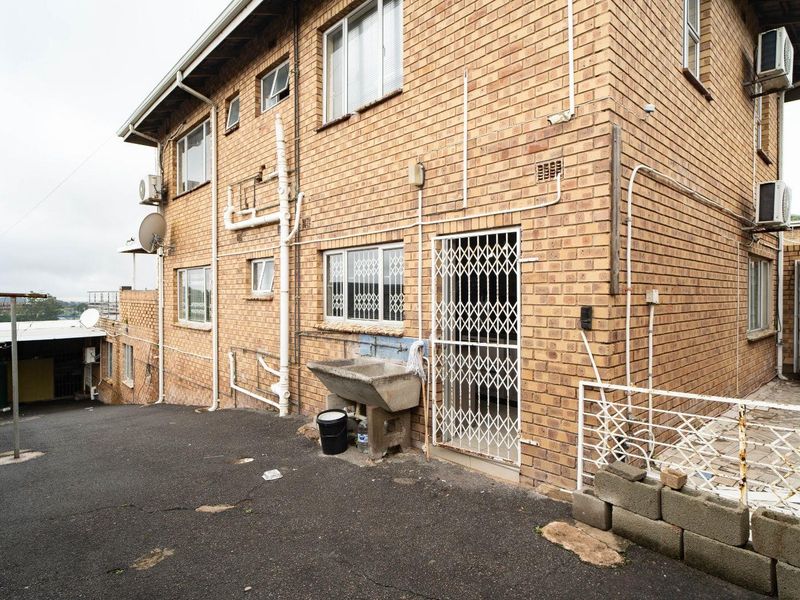 Rear exterior view of a face brick building featuring an external utility sink, security gates, and asphalt driveway area.