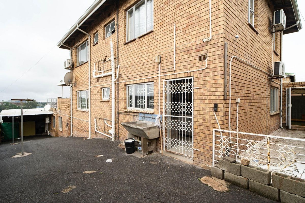Rear exterior view of a face brick building featuring an external utility sink, security gates, and asphalt driveway area.