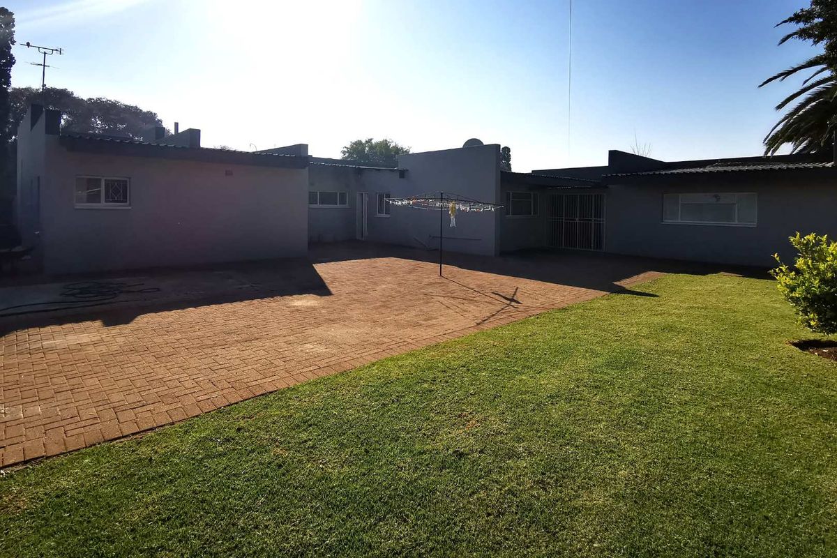 A spacious rear exterior view featuring a large paved courtyard, a well-maintained lawn, and secure window fittings.