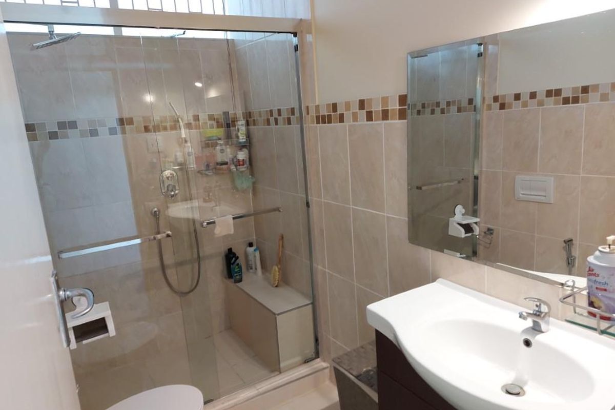 A functional bathroom featuring a glass-enclosed shower with built-in bench, a wall-mounted vanity with basin, and neutral wall tiling with decorative mosaic accents.