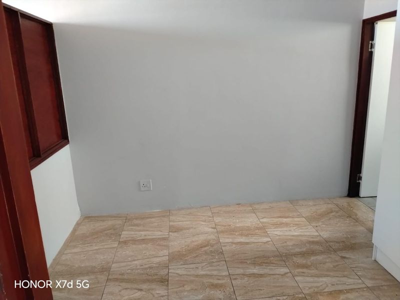 An empty bedroom featuring neutral wall finishes, tiled flooring, and dark timber door frames.