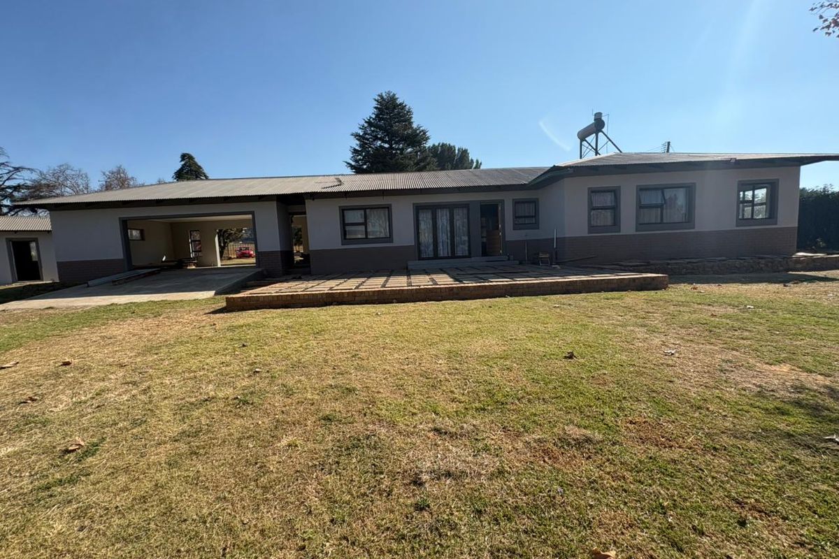 Rear view of the property featuring a large lawn, brick patio, open garage, and solar water heating system on a corrugated metal roof.