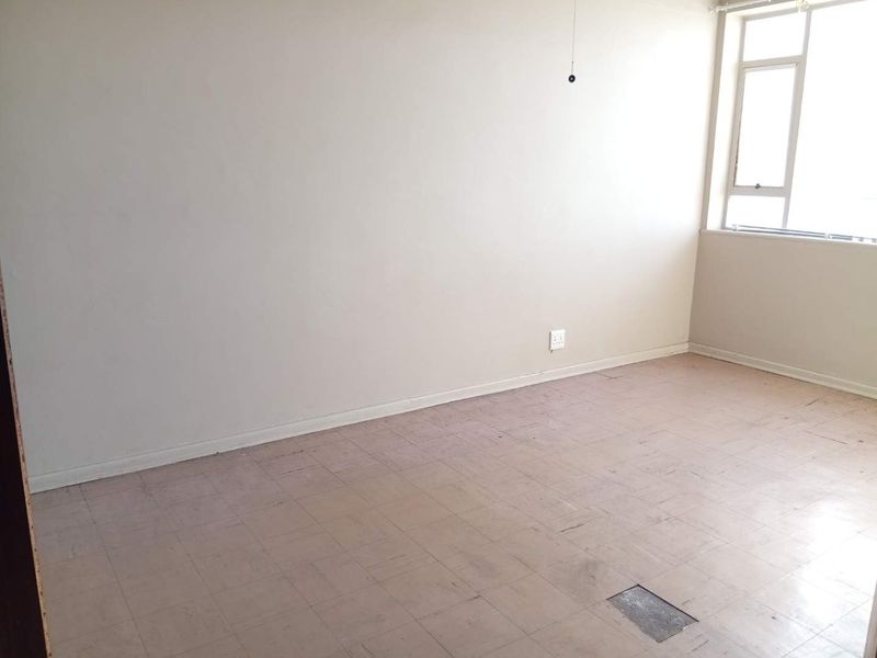 An empty bedroom featuring neutral walls, a large casement window, and worn vinyl tile flooring in need of replacement or refurbishment.