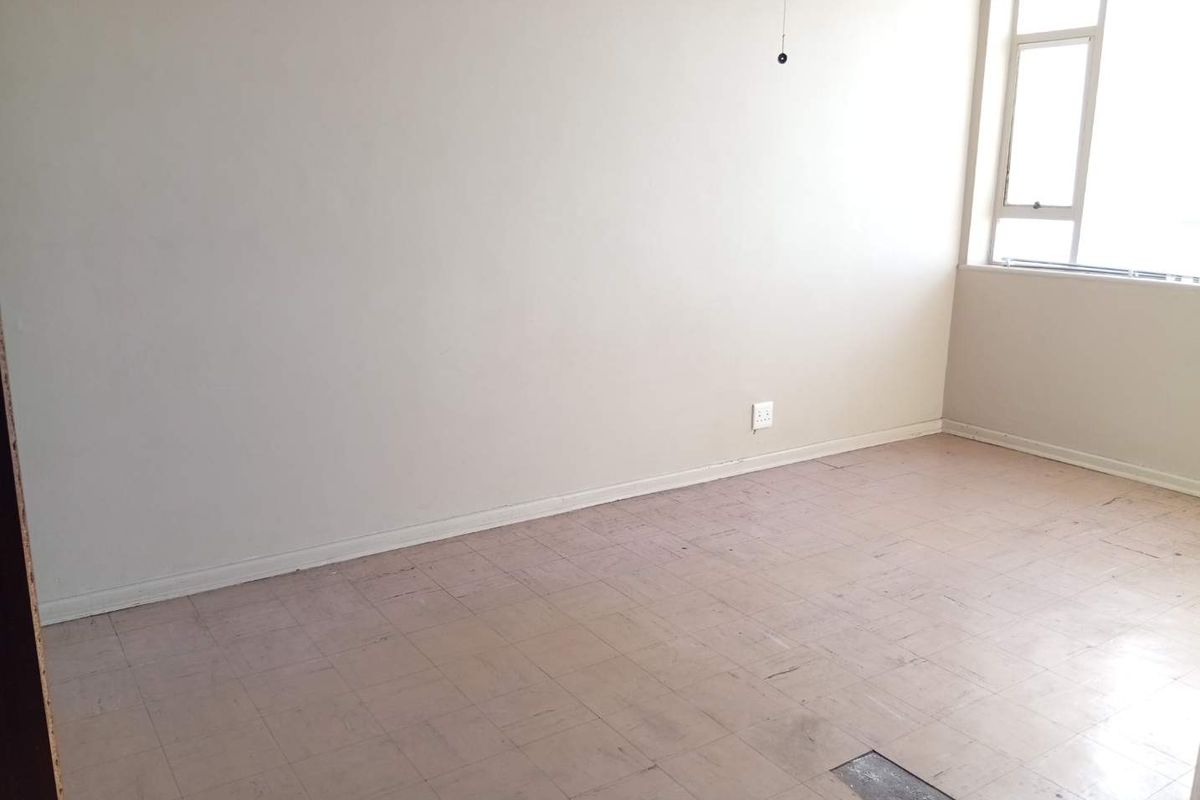 An empty bedroom featuring neutral walls, a large casement window, and worn vinyl tile flooring in need of replacement or refurbishment.