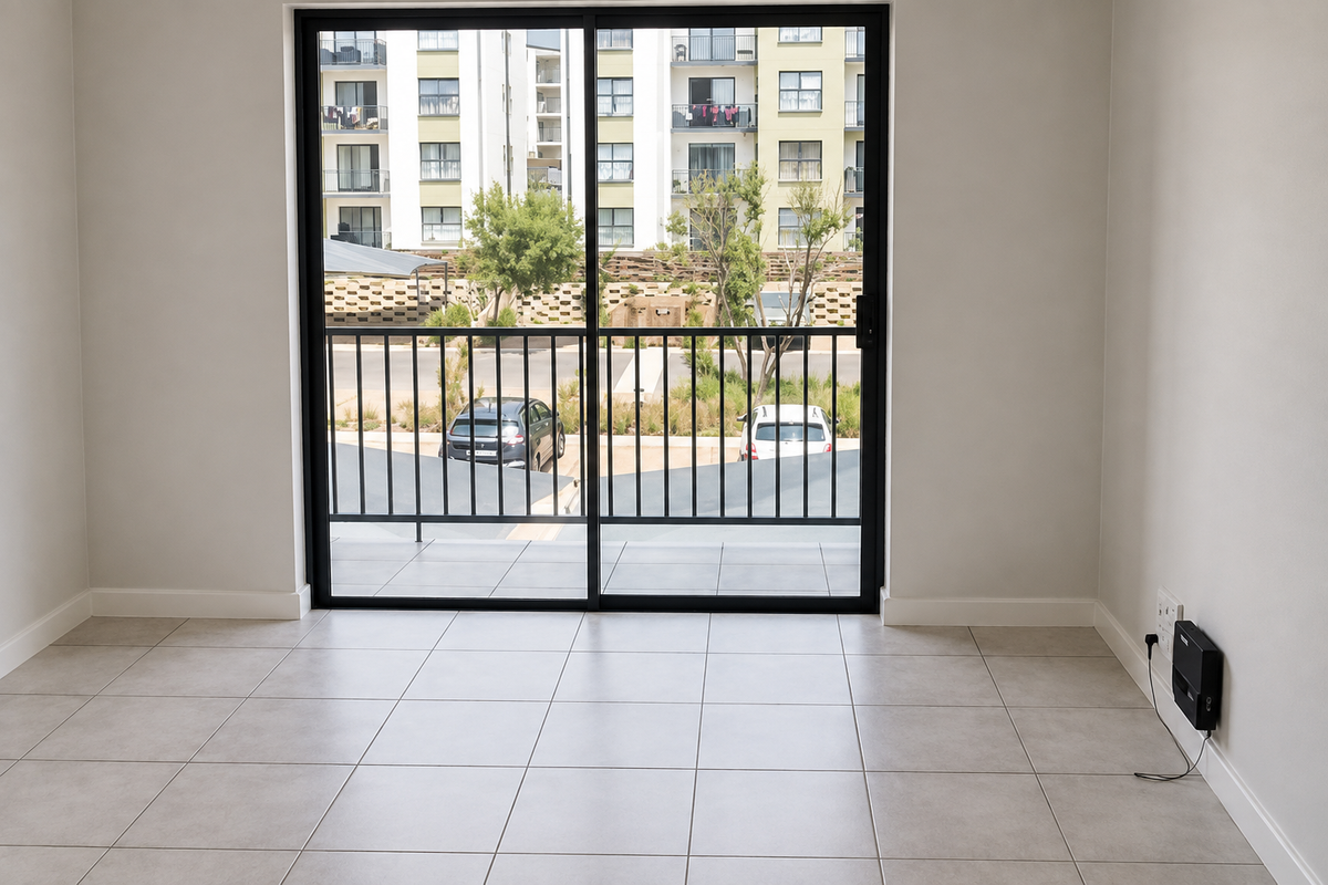 A bright, empty living area featuring neutral tiled flooring and a large sliding glass door providing access to an outdoor balcony.