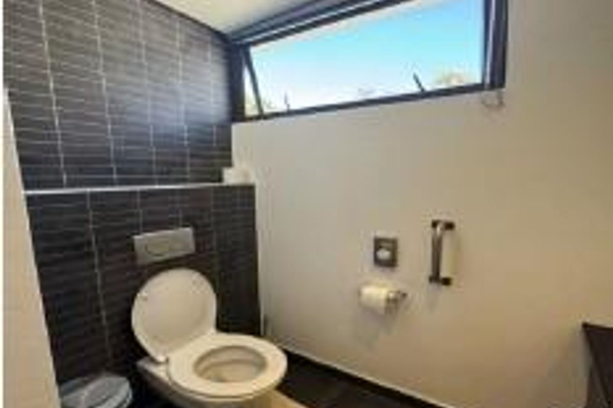A modern, accessible office restroom featuring a wall-mounted toilet, dark tiled accent wall, and a high-level awning window for natural light.