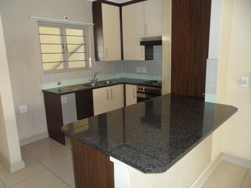 A clean, functional kitchen featuring granite countertops, built-in cabinetry, a hob, oven, and extractor fan with tiled flooring and backsplash.