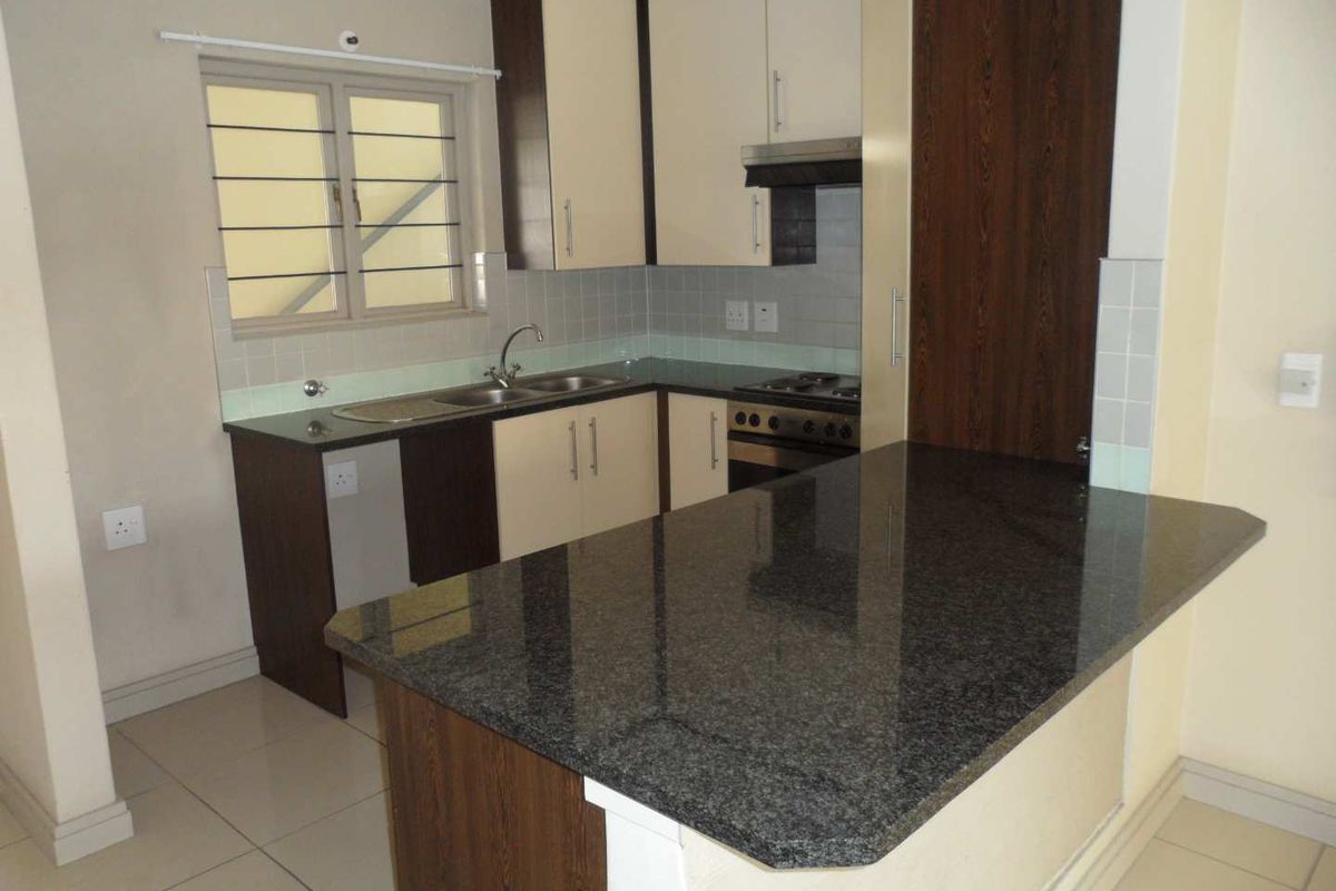 A clean, functional kitchen featuring granite countertops, built-in cabinetry, a hob, oven, and extractor fan with tiled flooring and backsplash.