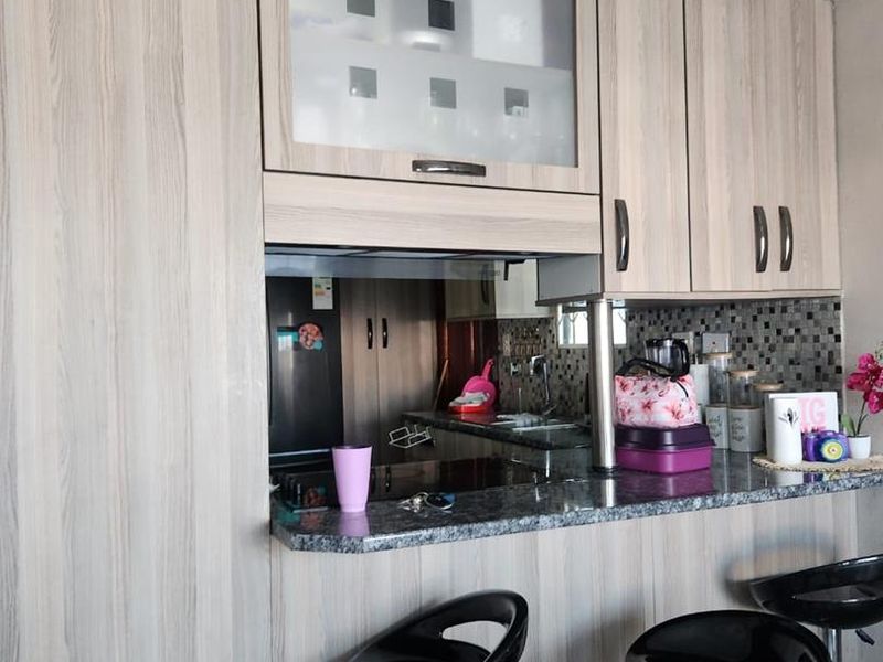 A functional kitchen featuring light wood-grain cabinetry, granite countertops, and a mosaic tile backsplash with a convenient breakfast bar area.