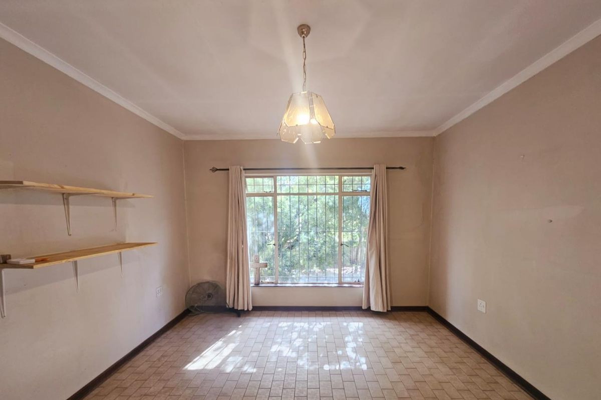 A simple, well-lit bedroom featuring tiled flooring, a large window with security bars, and built-in wall shelving.