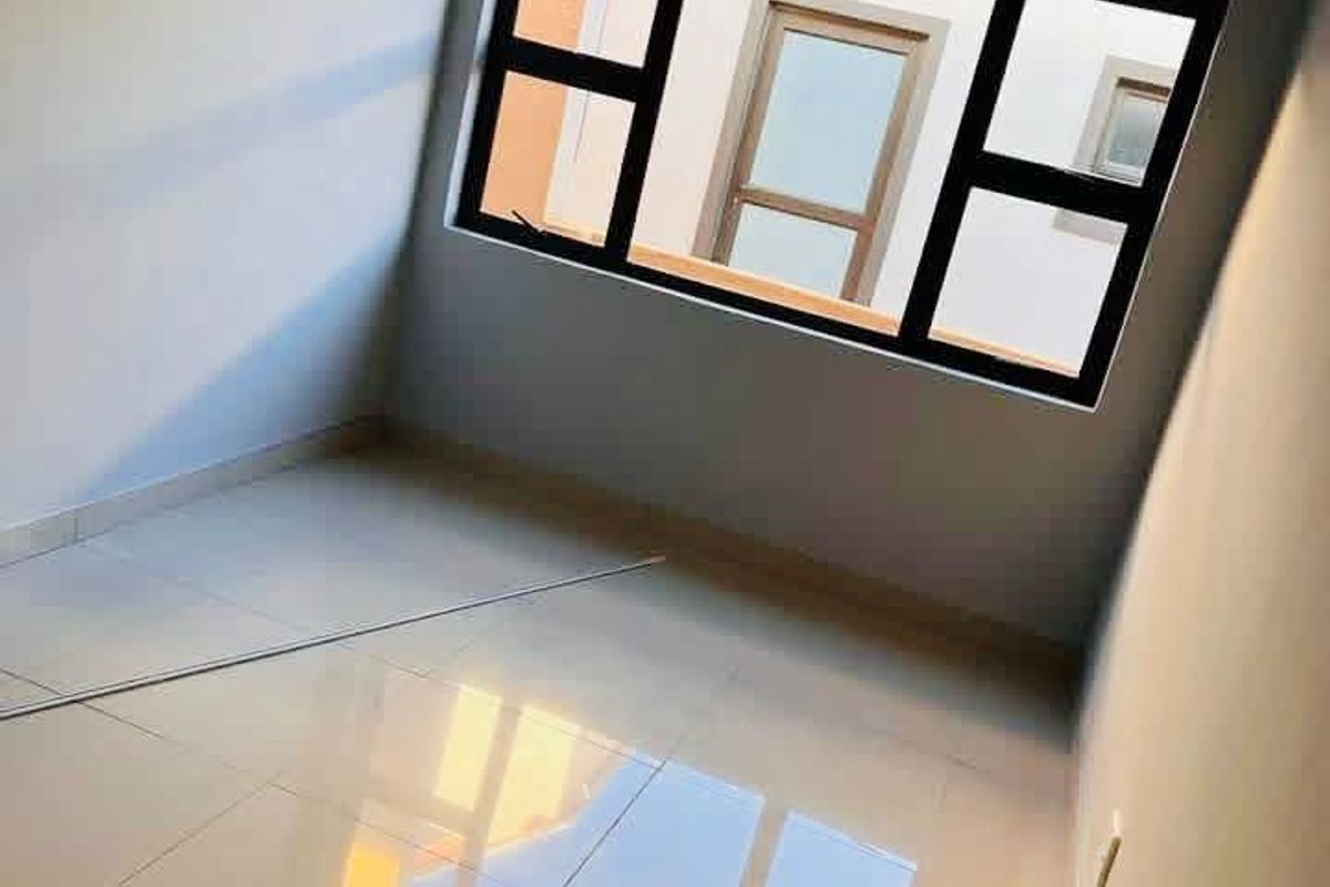 A bright, empty bedroom featuring modern tiled flooring and large aluminium-framed windows, offering a clean and neutral space ready for personalization.