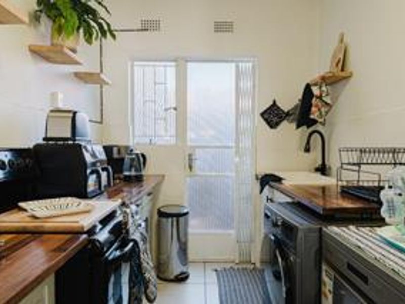 A compact kitchen featuring wooden countertops, a black faucet, and direct access to the exterior via a security gate.