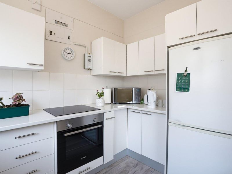 A compact, functional kitchen featuring white cabinetry, a modern electric hob, built-in oven, and a clean tiled backsplash.