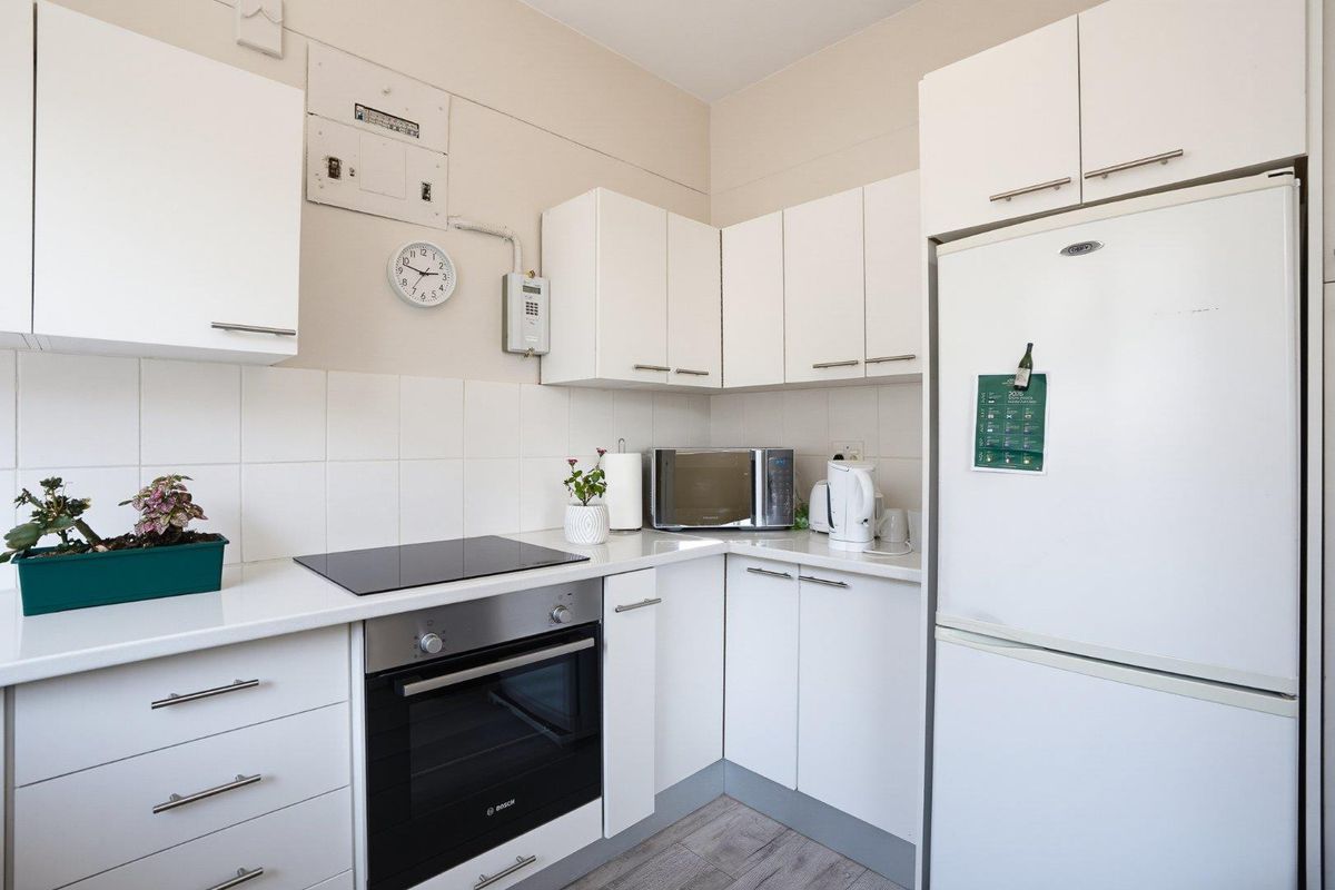 A compact, functional kitchen featuring white cabinetry, a modern electric hob, built-in oven, and a clean tiled backsplash.