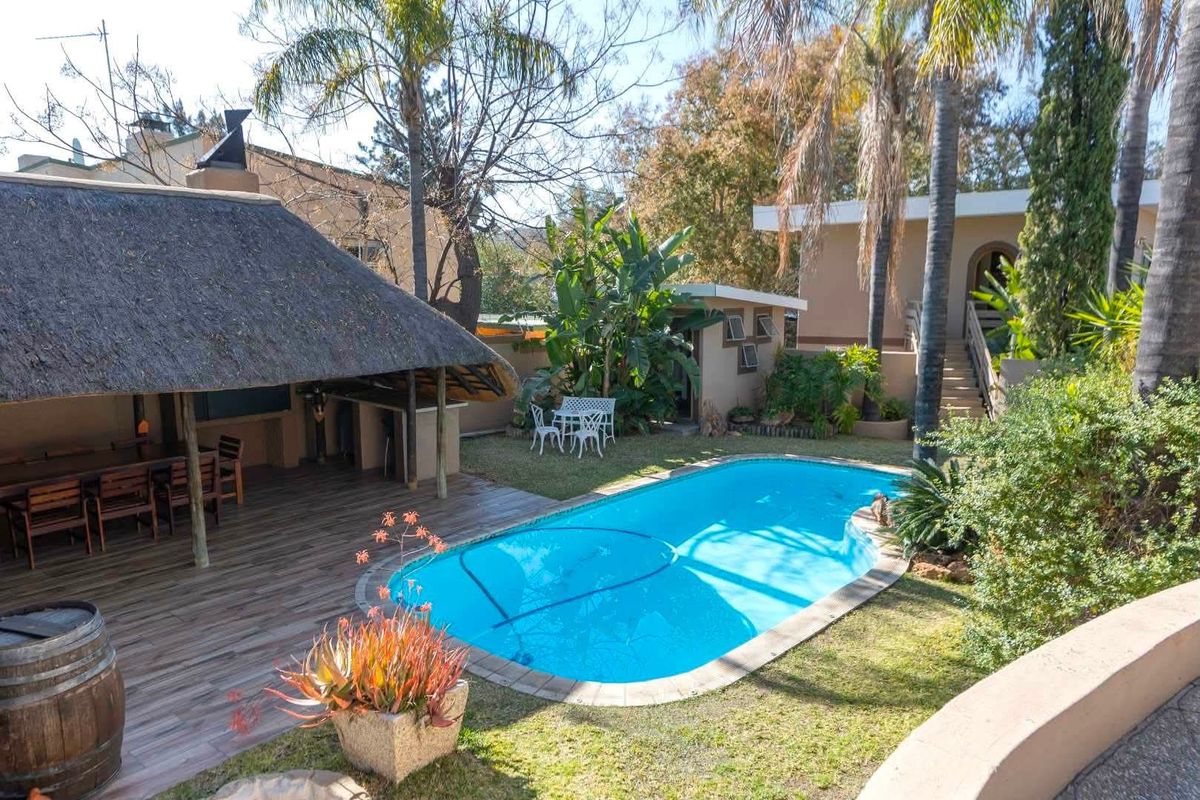 Outdoor entertainment area featuring a swimming pool, a covered thatched lapa with a built-in braai, and a landscaped garden setting.