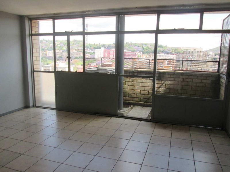 An empty living area featuring tiled flooring and large windows providing natural light and access to a balcony with urban views.