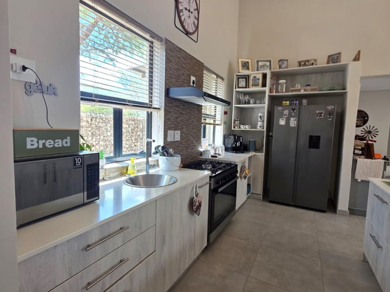 Modern kitchen featuring light wood-grain cabinetry, stone countertops, stainless steel sink, gas hob with extractor fan, and integrated shelving units.
