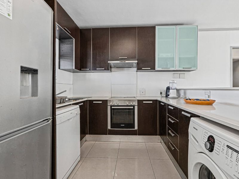 A functional kitchen featuring dark wood cabinetry, stone countertops, integrated oven, extractor fan, and tiled flooring, offering a clean and practical workspace.