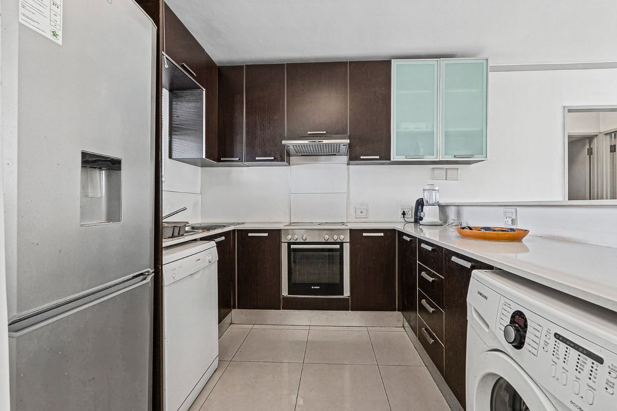 A functional kitchen featuring dark wood cabinetry, stone countertops, integrated oven, extractor fan, and tiled flooring, offering a clean and practical workspace.
