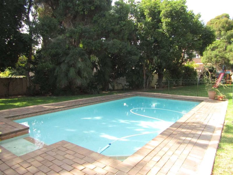 A well-maintained rectangular swimming pool surrounded by brick paving and established garden greenery, providing a private outdoor recreational space.