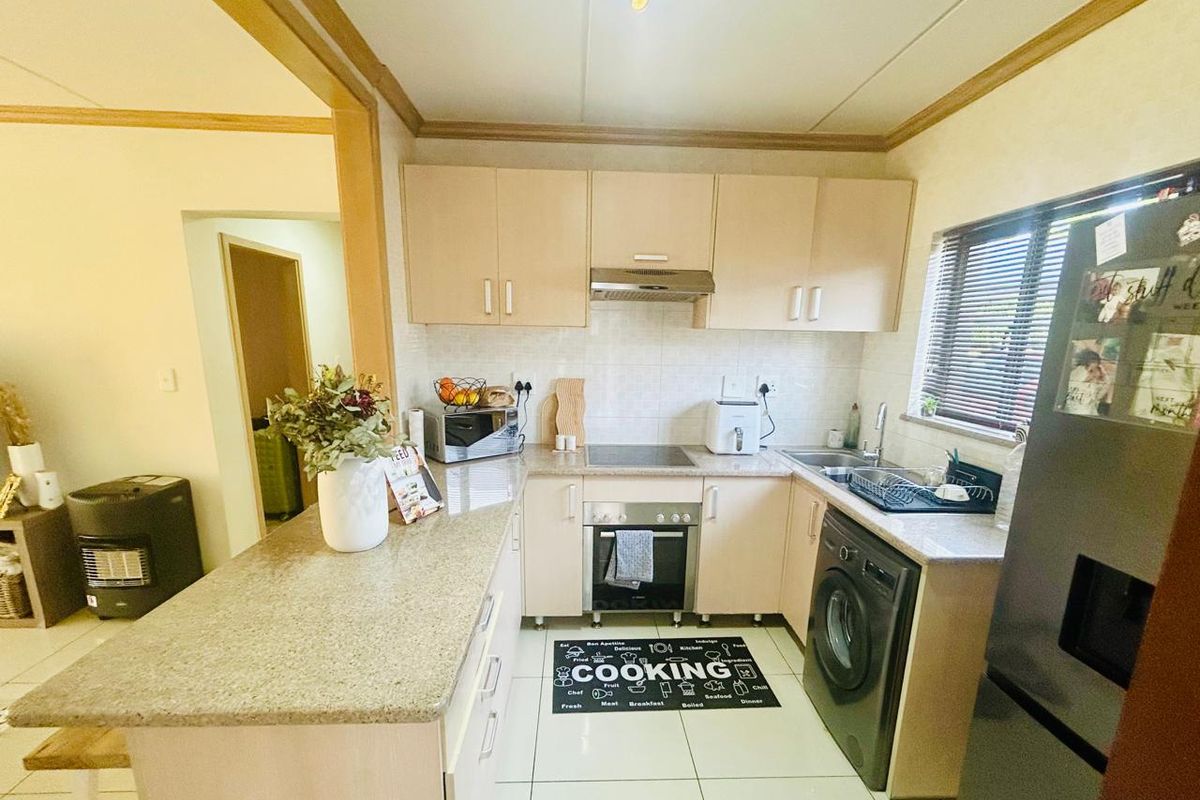 A functional kitchen featuring light-toned built-in cabinetry, laminate countertops, integrated oven and hob, and a breakfast nook, with tiled flooring throughout.