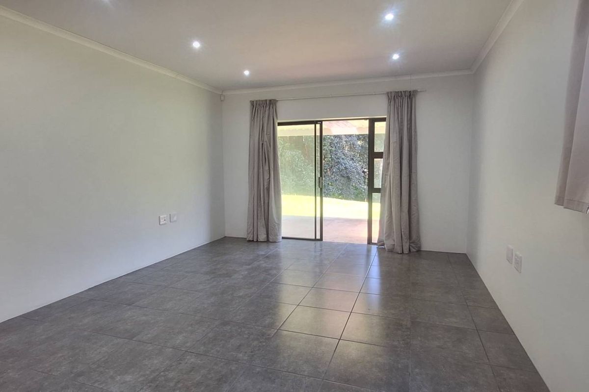 A bright, empty living room featuring modern grey floor tiles, recessed downlighting, and a sliding glass door providing access to the outdoor area.