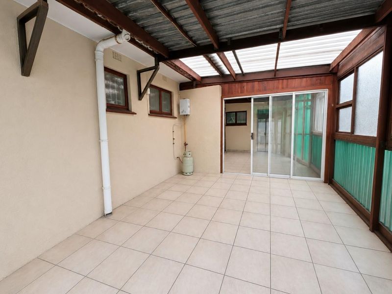 A covered patio area featuring tiled flooring, a timber pergola structure, and sliding glass doors providing access to the interior.