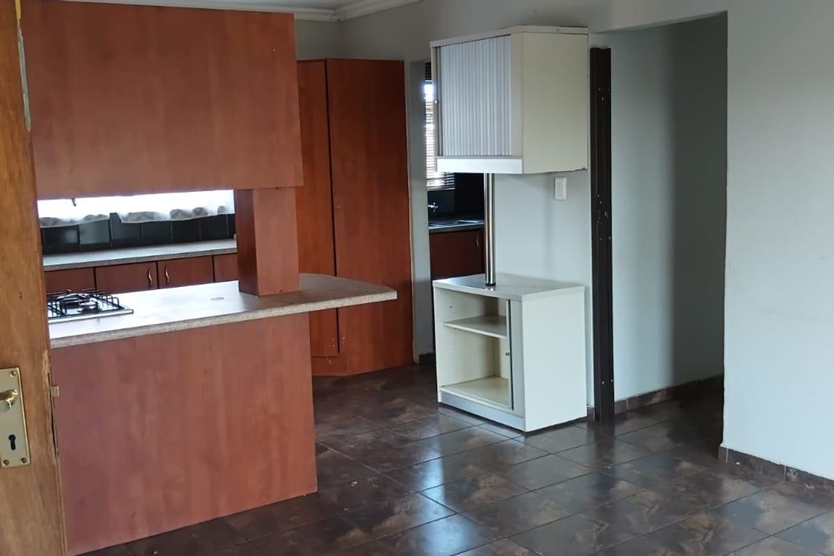A dated kitchen area featuring built-in wooden cabinetry, a gas hob, and tiled flooring, offering a functional layout ready for modernization.