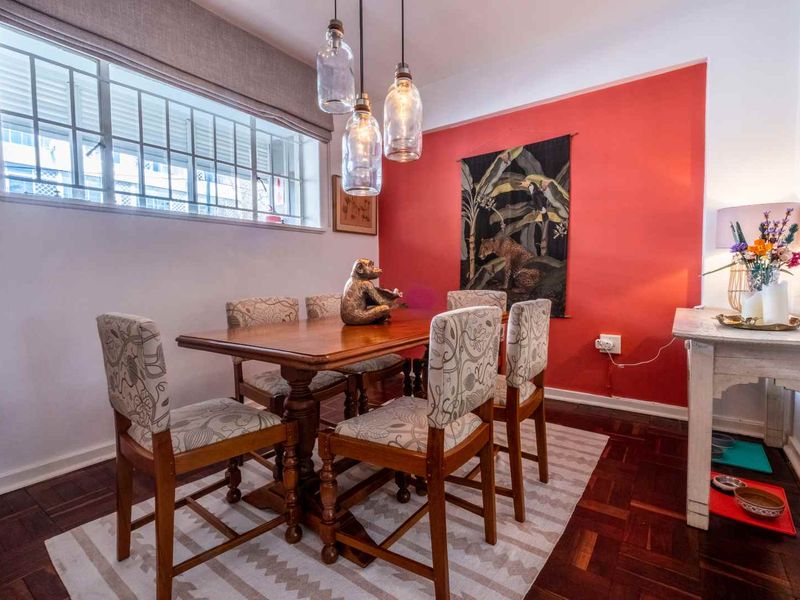 A well-lit dining room featuring classic parquet flooring, a bold accent wall, and modern pendant lighting, creating a warm and inviting atmosphere.